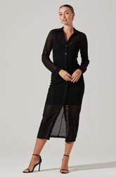 A woman is wearing a black, long-sleeved button-up dress made of a see-through, mesh fabric with a striped pattern. The dress has a collar and a front slit that reveals her legs. She is also wearing black high-heeled sandals with ankle straps.